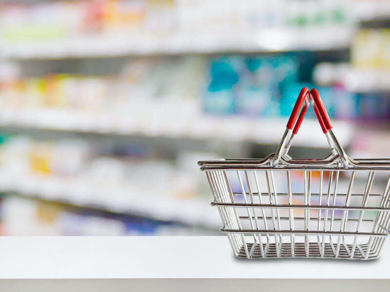 Empty shopping basket on pharmacy drugstore counter with blur shelves of medicine, over the counter hearing aids, and vitamin supplements background.